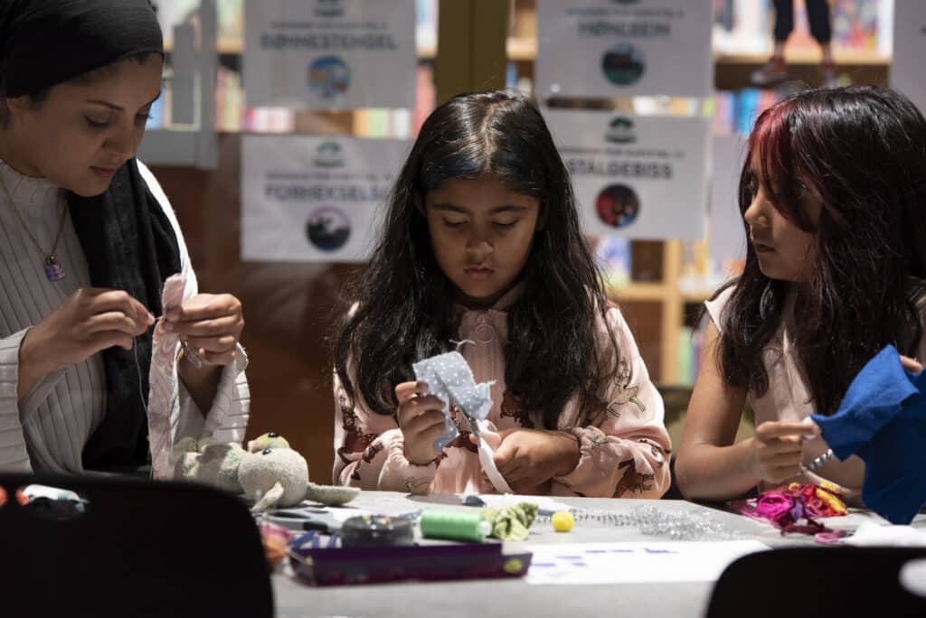 to barn og en voksen jobber med tekstiler ved et bord Deichman bibliotek