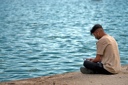 Bilde av en mann som sitter på ei brygge ved vannet