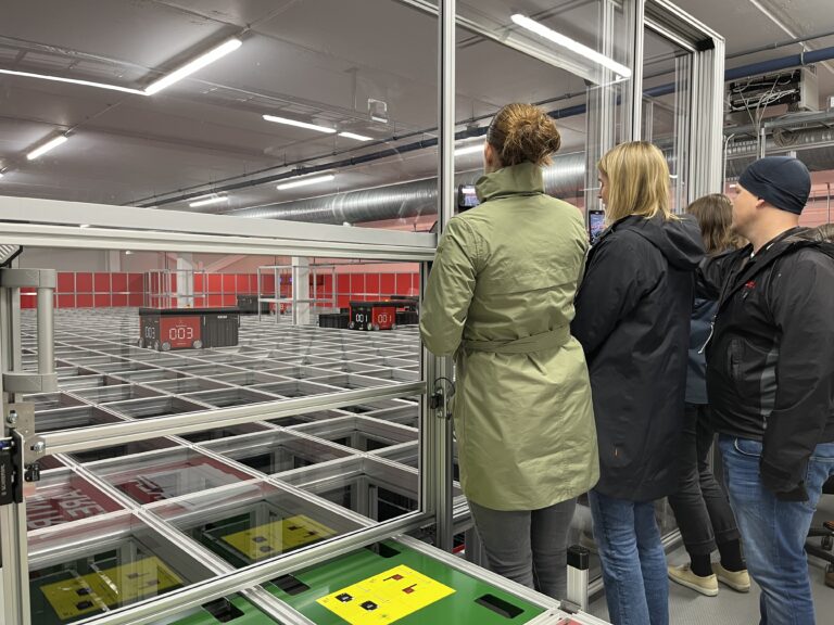 Mennesker ser på roboter som jobber på toppen av AutoStore