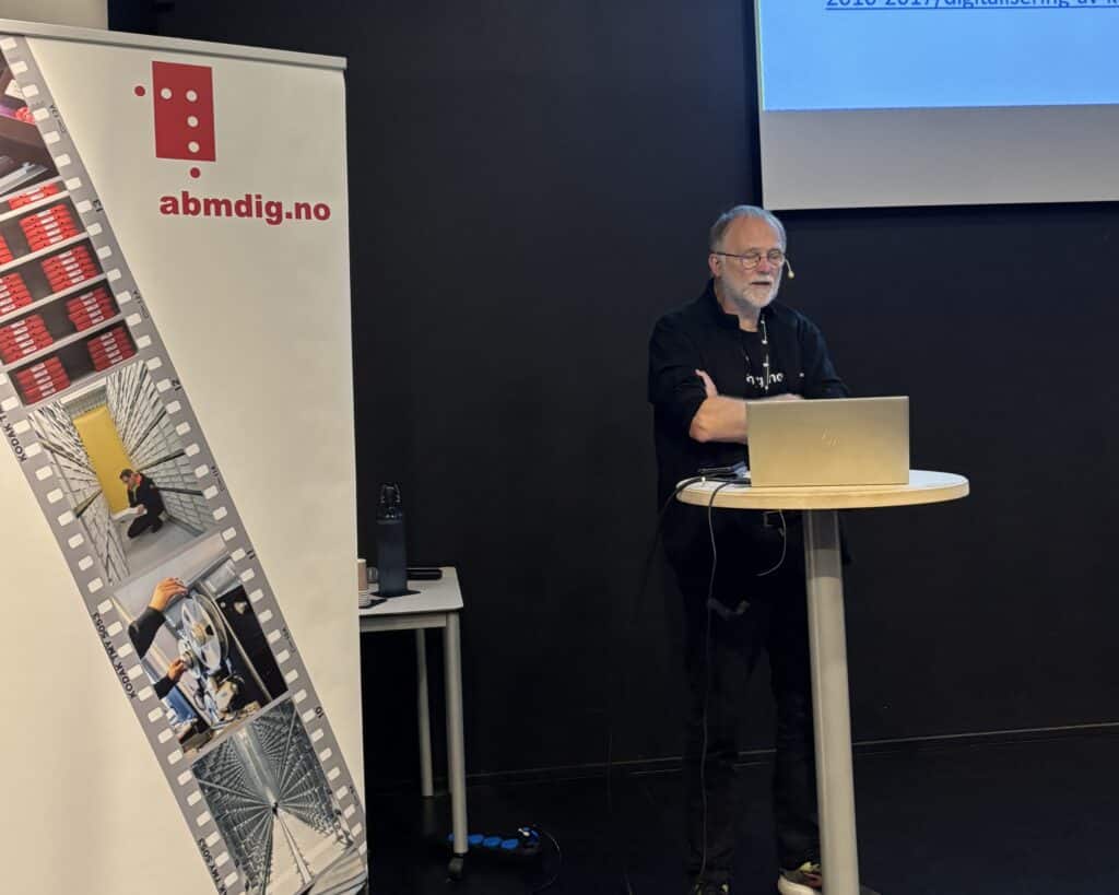 Foredragsholder står ved siden av roll-up med bilder og logo for abmdig.no