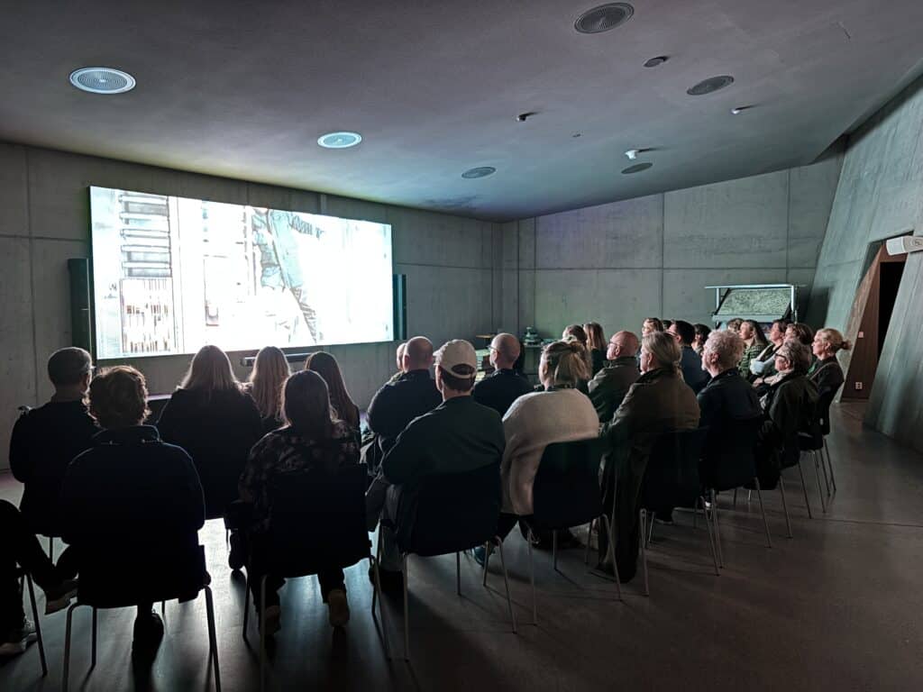 Publikum som sitter på stoler og ser på film på stor skjerm