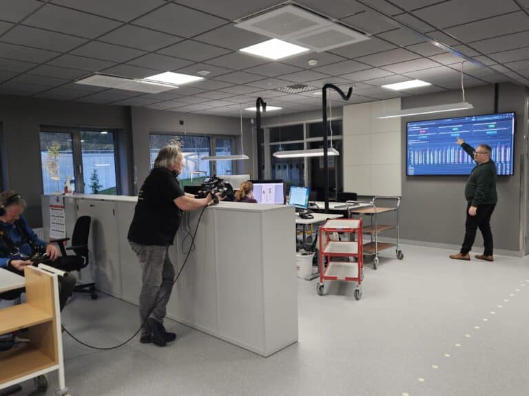 Kamerafolk filmer og peker på skjerm i kontorlandskap