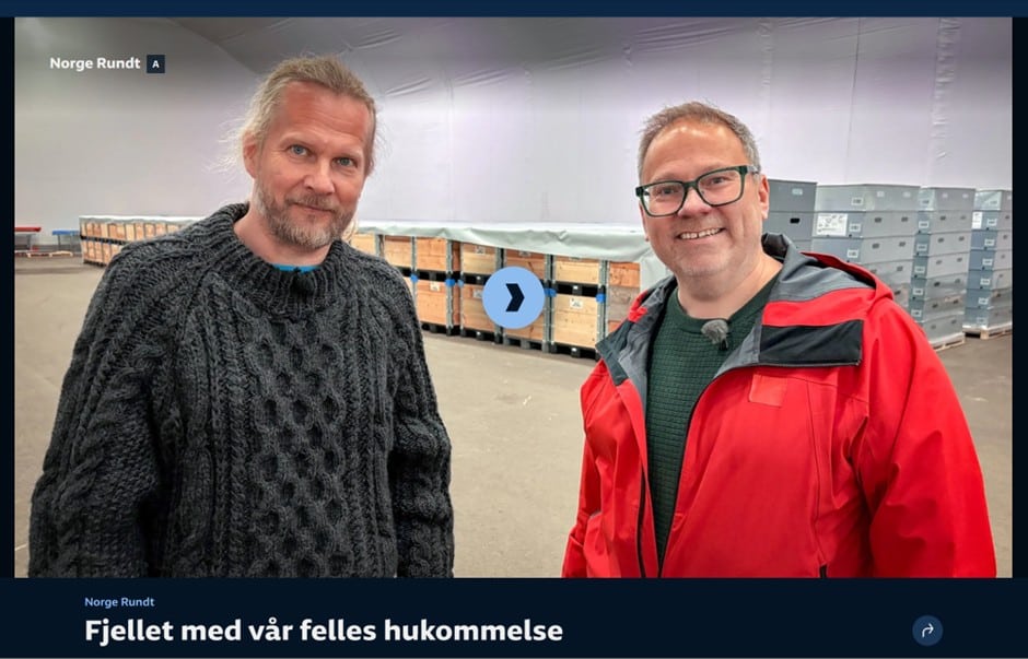 To menn foran en rekke med paller i en stor hall