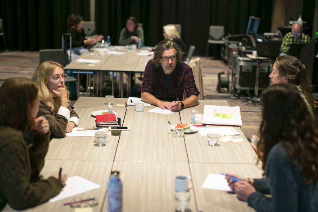 Foto av flere mennesker rundt et bord. Bildet illustrer en workshop og deltakerne sitter og tegner og diskuterer. 
