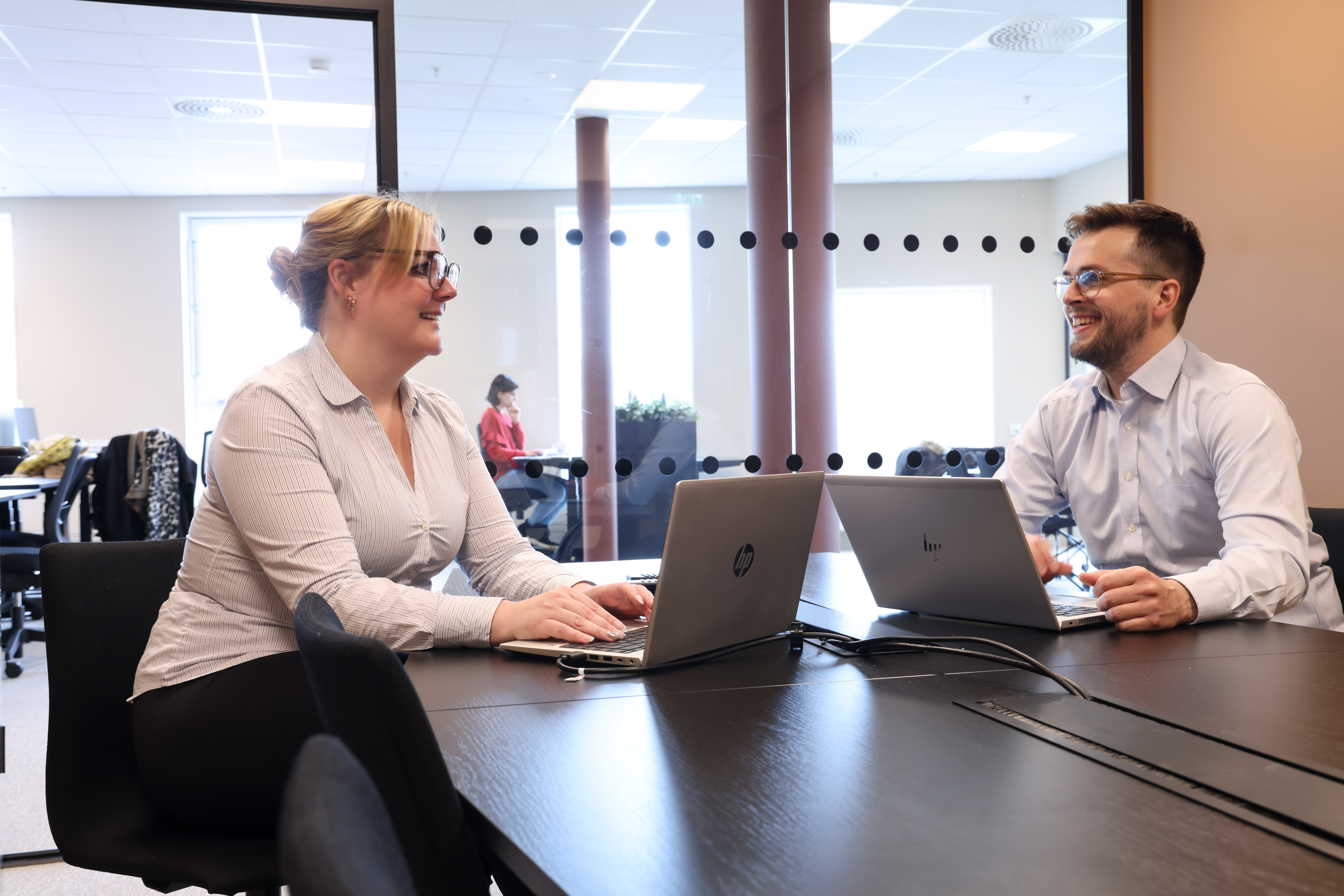To personer sitter ved et bord med hver sin datamaskin og snakker hyggelig sammen. Foto: Jørn Grønlund