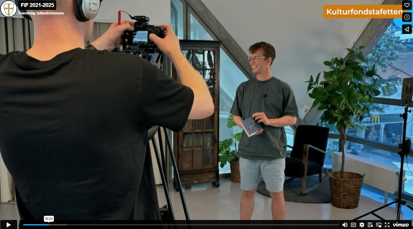 Skjermdump fra filmen. En mann filmer en som presenterer en kulturfondbok