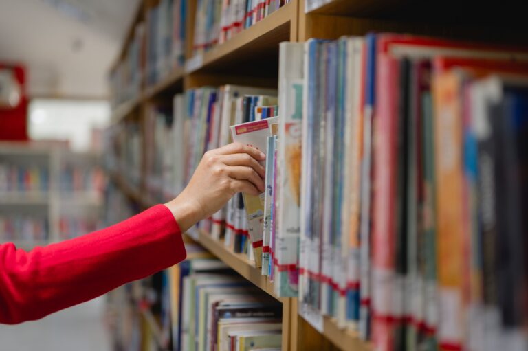 Arm som henter ut en bok fra bokhylle i biblioteket - shutterstock